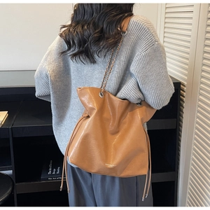 Rear view of model wearing a caramel brown drawstring tote bag with silver chain strap