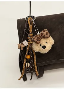 Close-up of plush dog charm with leopard bow and braided rope on a brown bag
