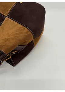Detail of suede patchwork bucket bag with white contrast stitching and gold metal hardware