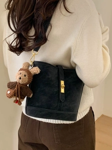 Retro black matte leather bucket bag with gold clasp and plush bunny charm on white sweater