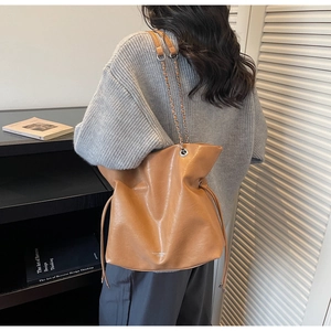 Close-up of caramel brown leather tote featuring metal chain strap and drawstring details