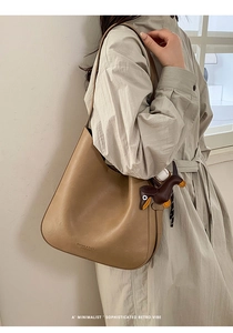 Detail view of khaki leather tote bag with brand logo and brown dachshund dog charm