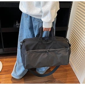 Detail of a large black travel bag with gray checkered front pocket and padded handles