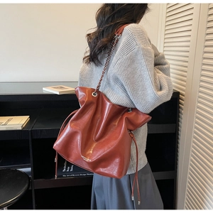 Close-up of rust red tote bag featuring drawstring detail and gold chain strap