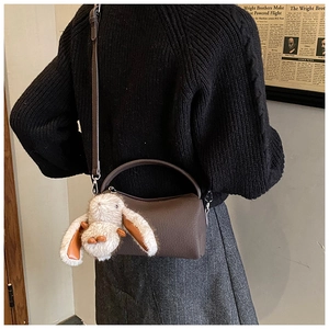 Detail of dark brown leather cylindrical crossbody bag with cute white rabbit charm accessory
