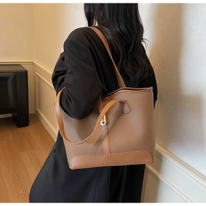 Detail of a large brown textured leather tote bag with gold metal buckle and reinforced base