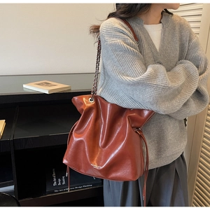 Caramel leather tote bag with chain strap and drawstring detail on female model