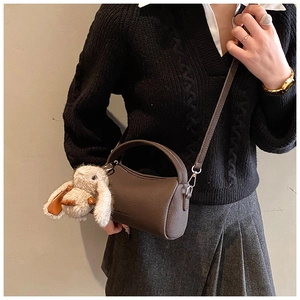 Detail of dark brown leather crossbody bag with a cute plush bunny charm and shoulder strap