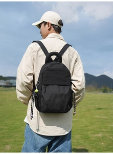 Détail du sac à dos noir avec panneau à carreaux porté par un modèle en extérieur