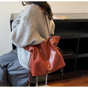 Detail of red-brown tote bag featuring silver chain strap and side drawstring design