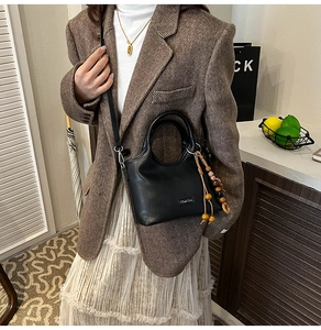 Detail of black matte leather bucket bag featuring bohemian wooden beads and top handle
