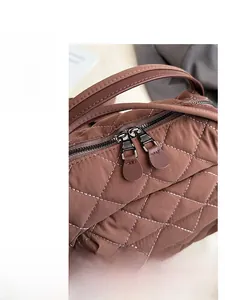 Detail of brown quilted bag with white stitching and dual metal zippers with leather pulls