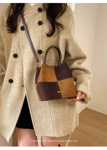 Detail of color-block suede bucket bag in brown and ginger worn with a beige coat