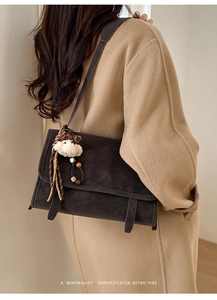 Model showing charcoal vintage messenger bag with teddy bear charm over a camel wool coat