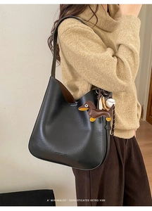 Detail of black leather tote bag with brown dachshund leather charm and baseball pendant