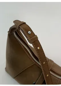 Detail of adjustable leather shoulder strap with silver eyelets on a brown suede bag