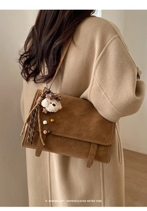 Close-up of retro brown leather crossbody bag featuring a plush bear and tassel charm