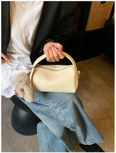 Detail of cream lychee texture leather handbag with a plush rabbit charm accessory