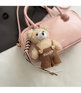 Detail of plush bear bag charm with beige faux fur and corduroy overalls on a pink purse