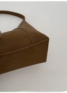 Detail view showing the wide bottom and structured leather texture of the brown handbag