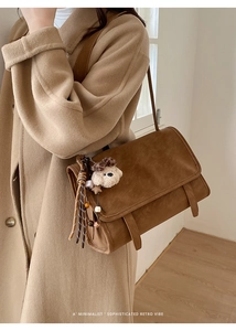 Detail of vintage brown messenger bag with plush bear charm and woven tassel accent