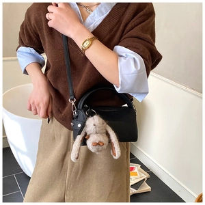 Detail of black mini crossbody bag with cute plush rabbit charm on a stylish model