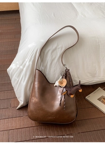 Detailed view of retro dark brown leather hobo bag with cute dog charms on a white bed
