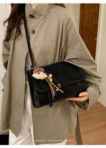 Detail of a retro black suede shoulder bag with a cute bear plush and tassel charm