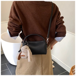 Detail of black pebbled leather Boston bag with cute plush rabbit charm on a model