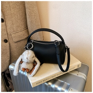 Detail of black lychee grain cylinder bag with cute bunny charm on silver suitcase
