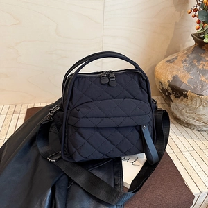 Detail of black quilted nylon handbag with dual handles and adjustable shoulder strap