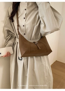 Close-up of minimalist brown crescent shoulder bag with retro buckle on cream trench coat