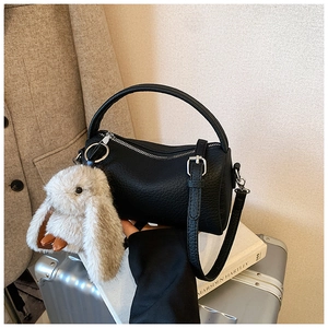 Detail of black pebbled leather handbag with plush rabbit charm on a silver suitcase