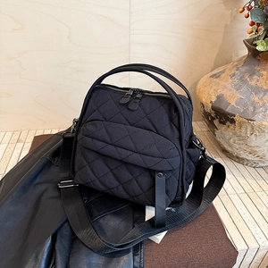 Detail of black quilted crossbody bag showing multiple zippers and wide strap
