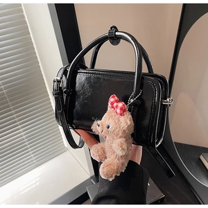 Detail of a black glossy leather handbag featuring a cute plush bear charm accessory