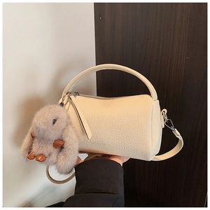 Detail view of cream leather cylinder bag with plush bunny charm on dark wood background