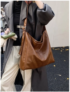 Detail view of a large brown leather tote bag with silver hardware on a street setting