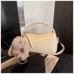 Detail of off-white leather cylinder bag with plush bunny charm and top handle