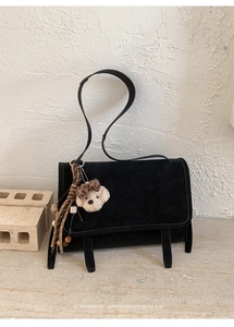 Detail of a black retro suede messenger bag with decorative straps and a plush dog charm
