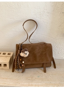 Detail of brown retro messenger bag with suede texture and plush puppy pendant
