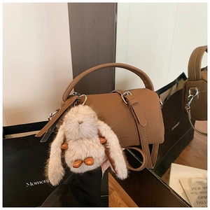 Close-up of brown litchi grain leather bucket bag with cute plush rabbit charm