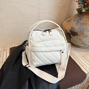 Close-up of white quilted tote bag featuring wide strap and dual zipper detail