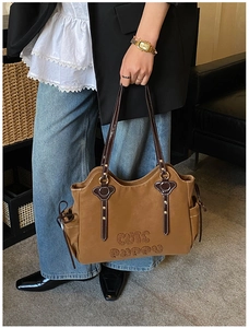 Detail of brown tote bag with CUTE PUPPY text, leather straps, and rivet accents