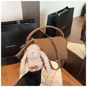 Brown cylindrical bucket bag with lychee texture, top handle, and cute plush rabbit charm