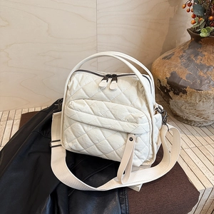 Detail of cream quilted shoulder bag with wide strap and vintage hardware accents