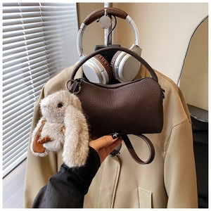 Detail of dark brown pebble leather cylinder bag with plush rabbit charm and crossbody strap
