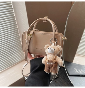 Detail of beige square handbag with brand embossing and cute teddy bear charm accessory