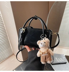 Detailed macro view of black glossy leather handbag with teddy bear charm and logo