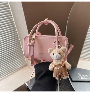 Detailed shot of a pink glossy square bag with a cute bear charm and shoulder strap