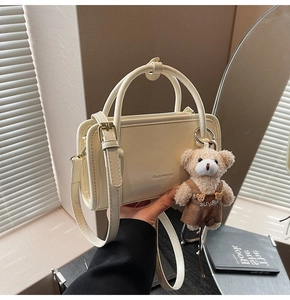 Detail of cream white structured tote bag with a plush bear charm and thin shoulder strap
